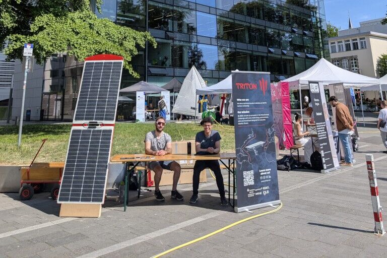 Two team members at our stand with a solar panel and the Triton banner